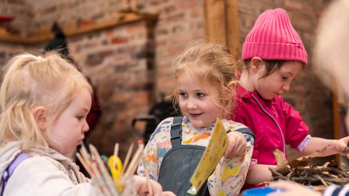 Three children taking part in crafts at a table, including paper, card and sticks